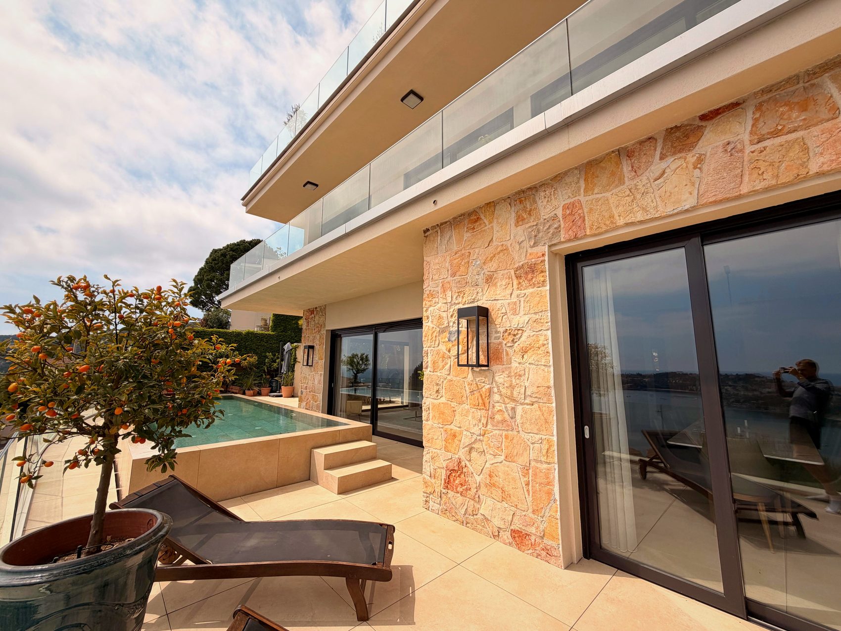 Façade en pierre, verre et terrasse de la piscine au soleil de l'après-midi